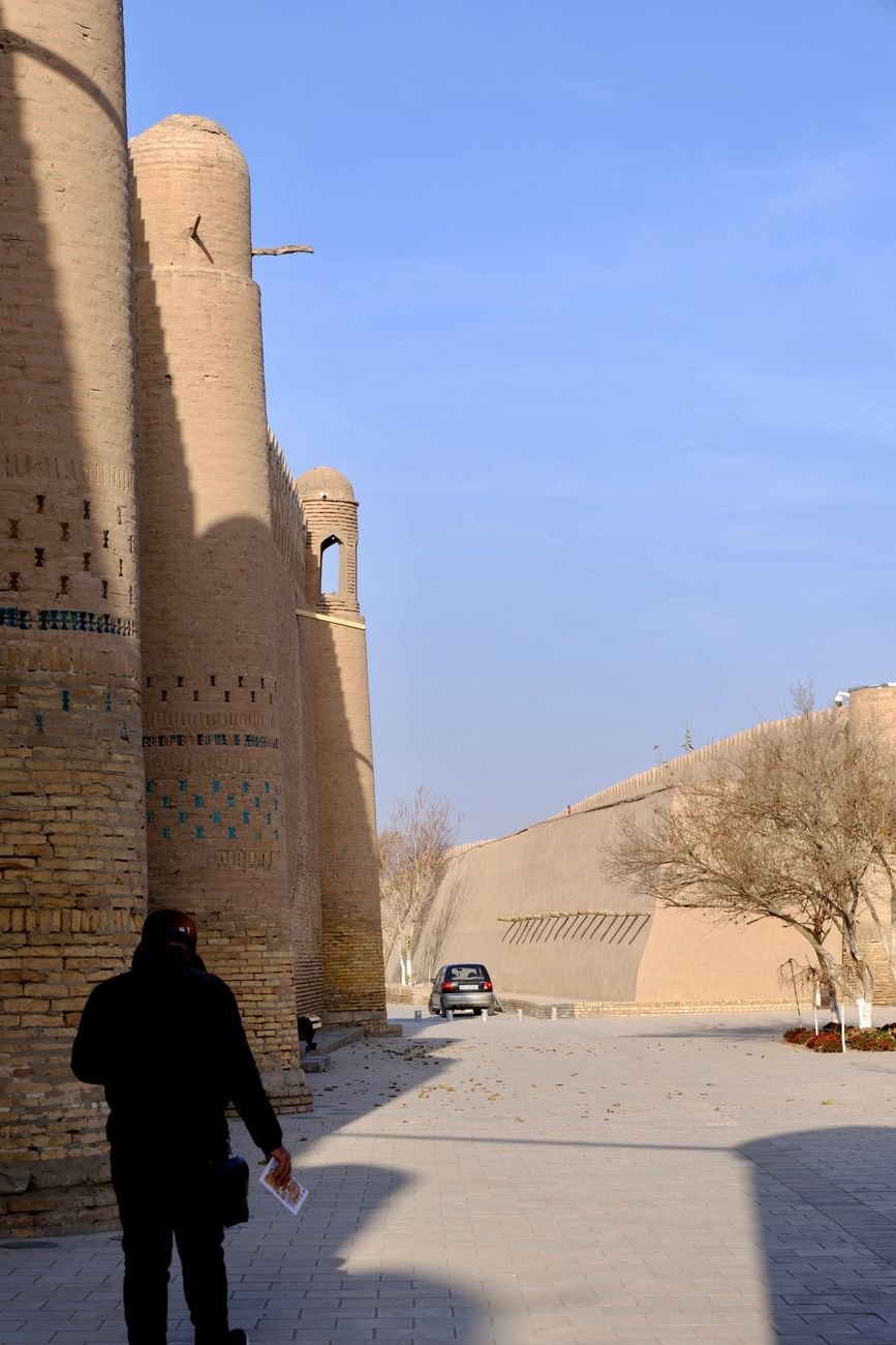 A person walks near the historic mudbrick walls of Khiva, Uzbekistan, bathed in sunlight