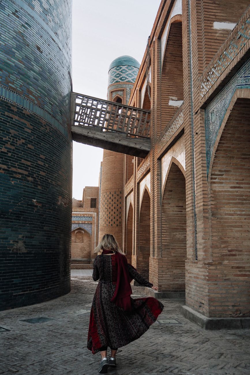 A woman in traditional attire walks near the historic Kalta Minor Minaret in Khiva, Uzbekistan