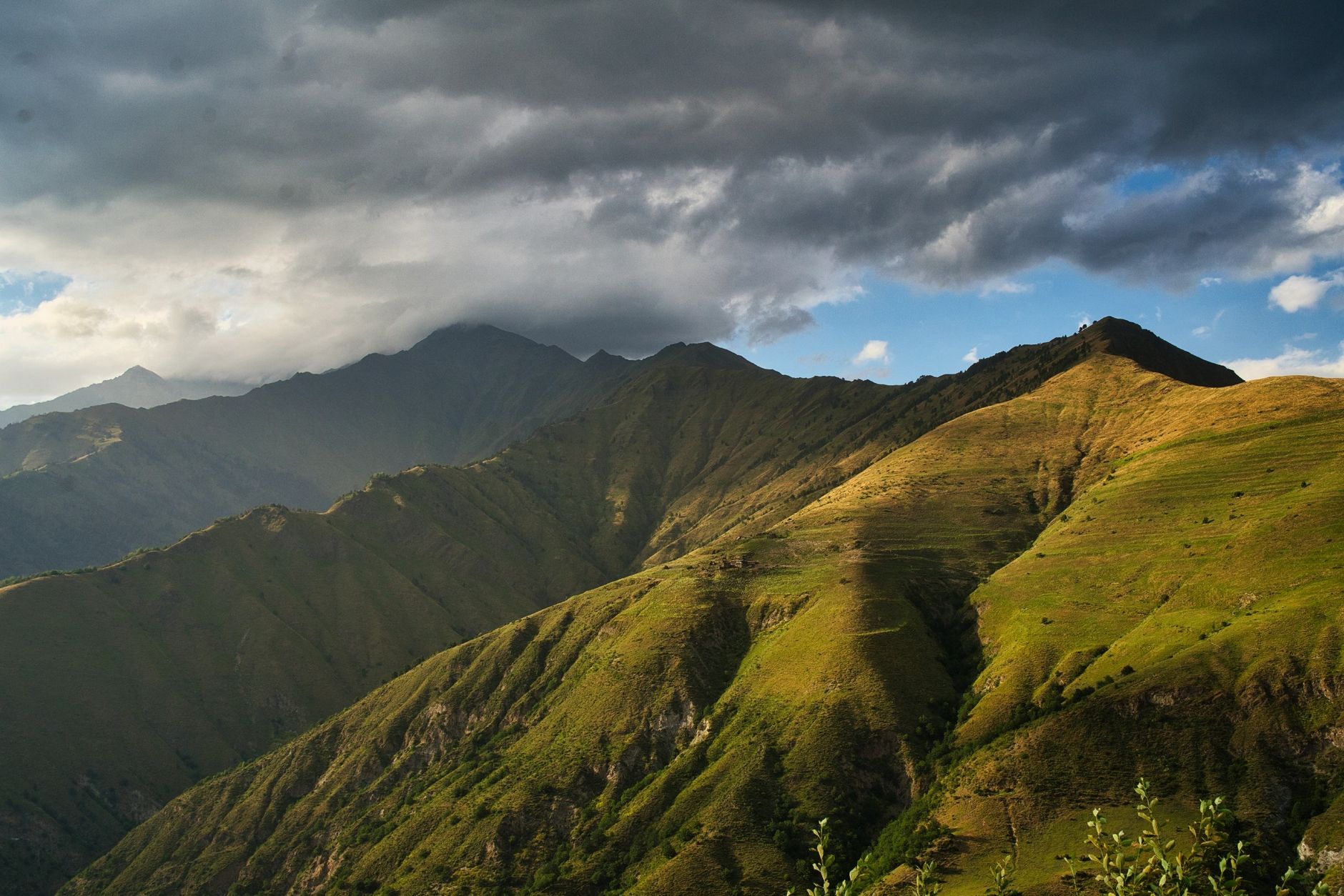 Green hills and mountains under a dynamic cloudy sky, showcasing the beauty of nature · Fann Mountains, Tajikistan, Uzbekistan