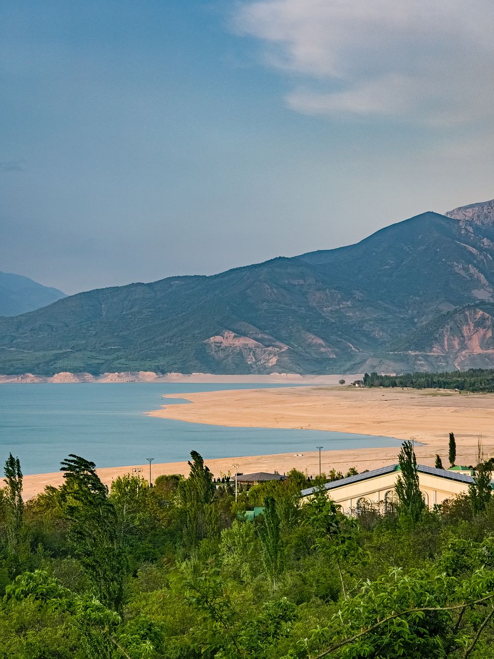 Sandy beach surrounded by lush greenery and majestic mountains under a serene sky · Nurata & Aydarkul, Uzbekistan