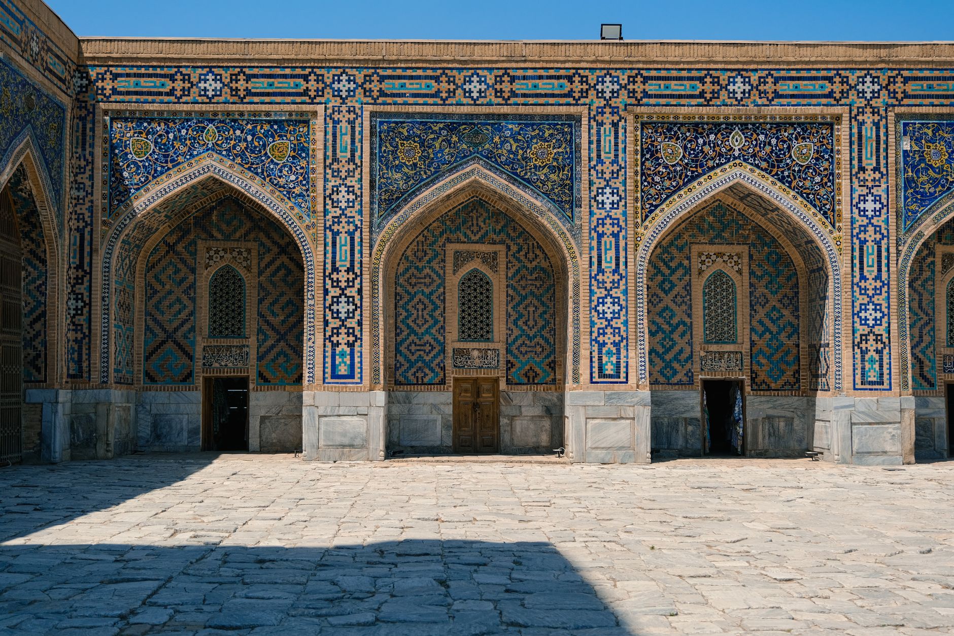 Beautifully detailed façade of a historic building with Islamic tiles and arches under a clear blue sky, Uzbekistan