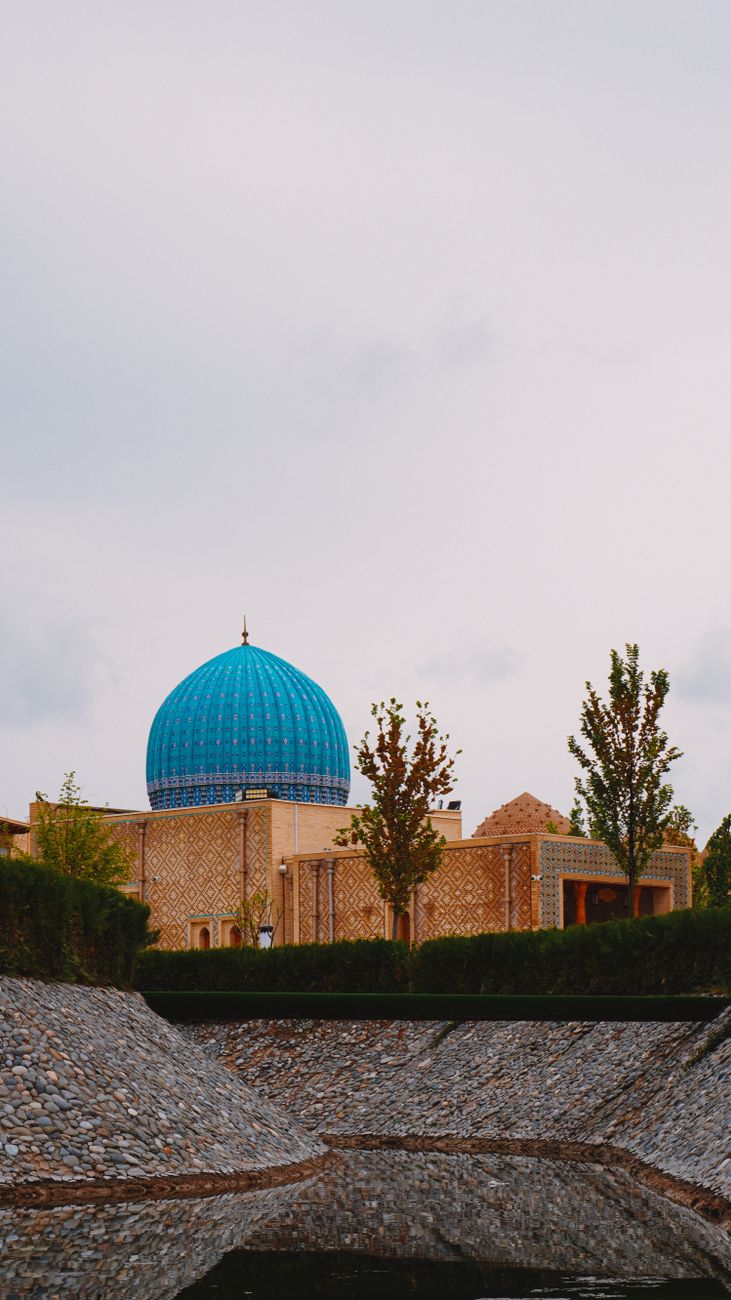 Blue dome of a historical mosque in Samarkand, Uzbekistan, surrounded by lush greenery
