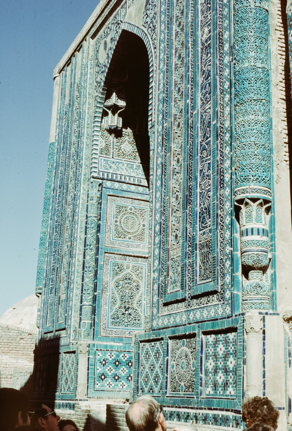 Turquoise-blue tile mosaic on a medieval Shah-i-Zinda mausoleum in Samarkand, showing arabesques, Kufic panels, and a slender columnar buttress